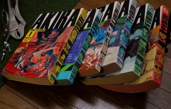 A complete six-volume set of the original Japanese 'Akira' manga by Katsuhiro Otomo, displayed in a stack with distinct colored spines and detailed cover art, sitting next to a pair of metal pliers on a wooden surface, representing how Tsumino Blog highlights iconic and rare manga collections.